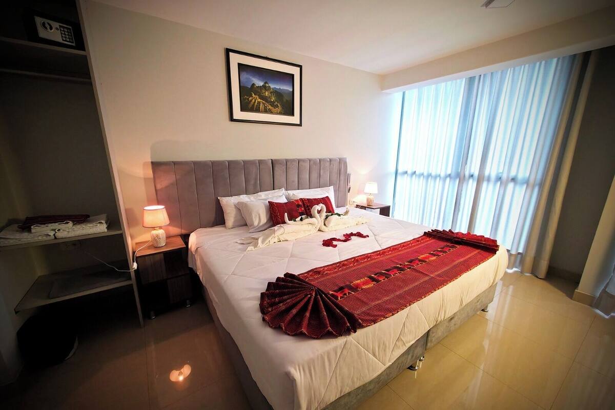 Una camera d'albergo con un letto, un comodino, una lampada, un quadro appeso al muro e una finestra con tende.