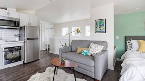 A modern apartment with a kitchenette, grey sofa, and a bed with white bedding. - Seattle Guesthouse: Downtown Access + Peaceful Retreat (Seattle)