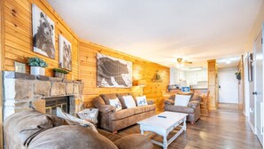 Un salon chaleureux avec une cheminée, des murs en bois et une cuisine à l’arrière-plan.