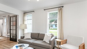 Een moderne woonkamer met een grijze bank, een witte fauteuil en een kleine tafel met een lamp.