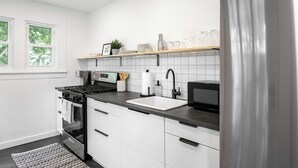 Een moderne keuken met witte kasten, een roestvrijstalen koelkast, een inbouwoven, een magnetron en een zwart aanrecht.