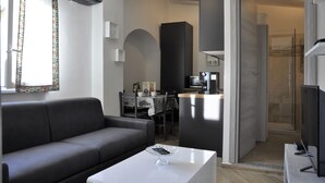 A modern living room with a grey sofa, a white coffee table, and a kitchen area in the background. - Elena House - Mareri apartments (Villa Faraldi)
