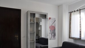 A modern living room with a grey sofa, a built-in shelving unit, a dark wooden door, and a window with patterned curtains. - Elena House - Mareri apartments (Villa Faraldi)