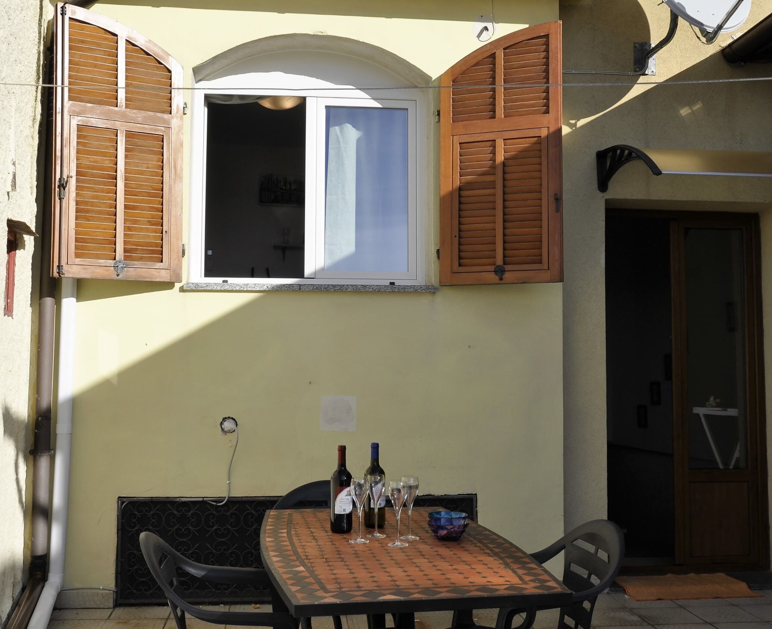 Un pequeño espacio exterior con comedor, una mesa dispuesta para dos personas, con dos botellas de vino y varios vasos.