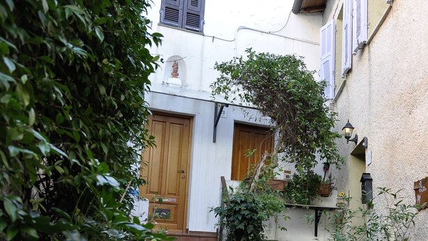 A narrow courtyard with a wooden door, a white wall, and a small garden area with plants and a butterfly. - Elena House - Mareri apartments (Villa Faraldi)