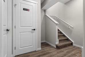 Una puerta blanca con un cartel que dice "Restricted Area", una escalera de madera con barandillas blancas y un piso de madera.
