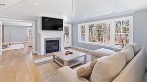 A spacious living room with a fireplace, a large window, and a flat-screen TV. - Olivia's Oasis: 006-HL - Stunning New Construction with Heated Pool & Hot Tub in Harwich (Harwich)