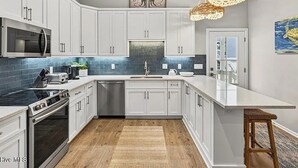 A modern kitchen with white cabinets, a stainless steel range, a microwave, and a dishwasher. - Sea + Second | Pool & Short Walk to the Beach (Ocean Isle Beach)