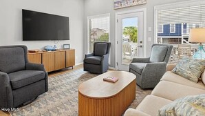 A modern living room with a flat-screen TV, two grey sofas, a wooden coffee table, and a ceiling fan. - Sea + Second | Pool & Short Walk to the Beach (Ocean Isle Beach)