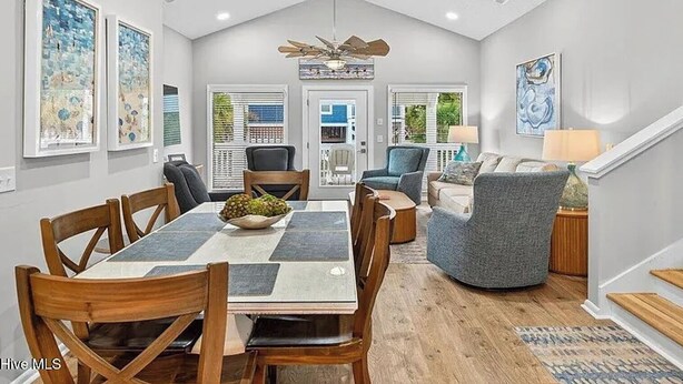 A spacious dining area with a high ceiling, a central chandelier, and a view of the outdoors through a door. - Sea + Second | Pool & Short Walk to the Beach (Ocean Isle Beach)