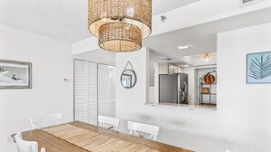 A modern dining area with a wooden table, white chairs, a woven rug, and a hanging light fixture. - 403 Sandcastle North Beach front (Indian Rocks Beach)
