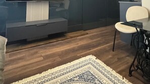 A modern living room with a large flat-screen TV, dark wood flooring, a patterned rug, and a minimalist design. - Premium Smart Studio with RiverView (T'bilisi)