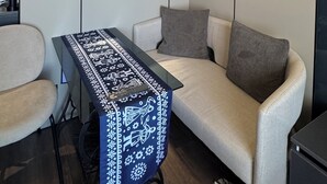 A modern room with a sofa, a small table with a patterned tablecloth, a wall-mounted air conditioner, and framed artwork. - Premium Smart Studio with RiverView (T'bilisi)