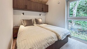 Een slaapkamer met een groot bed, houten kasten erboven en een raam met uitzicht op groen.