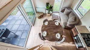 Een ruime woonruimte met een ronde houten tafel, een grijze bank en een trap naar een verdieping.