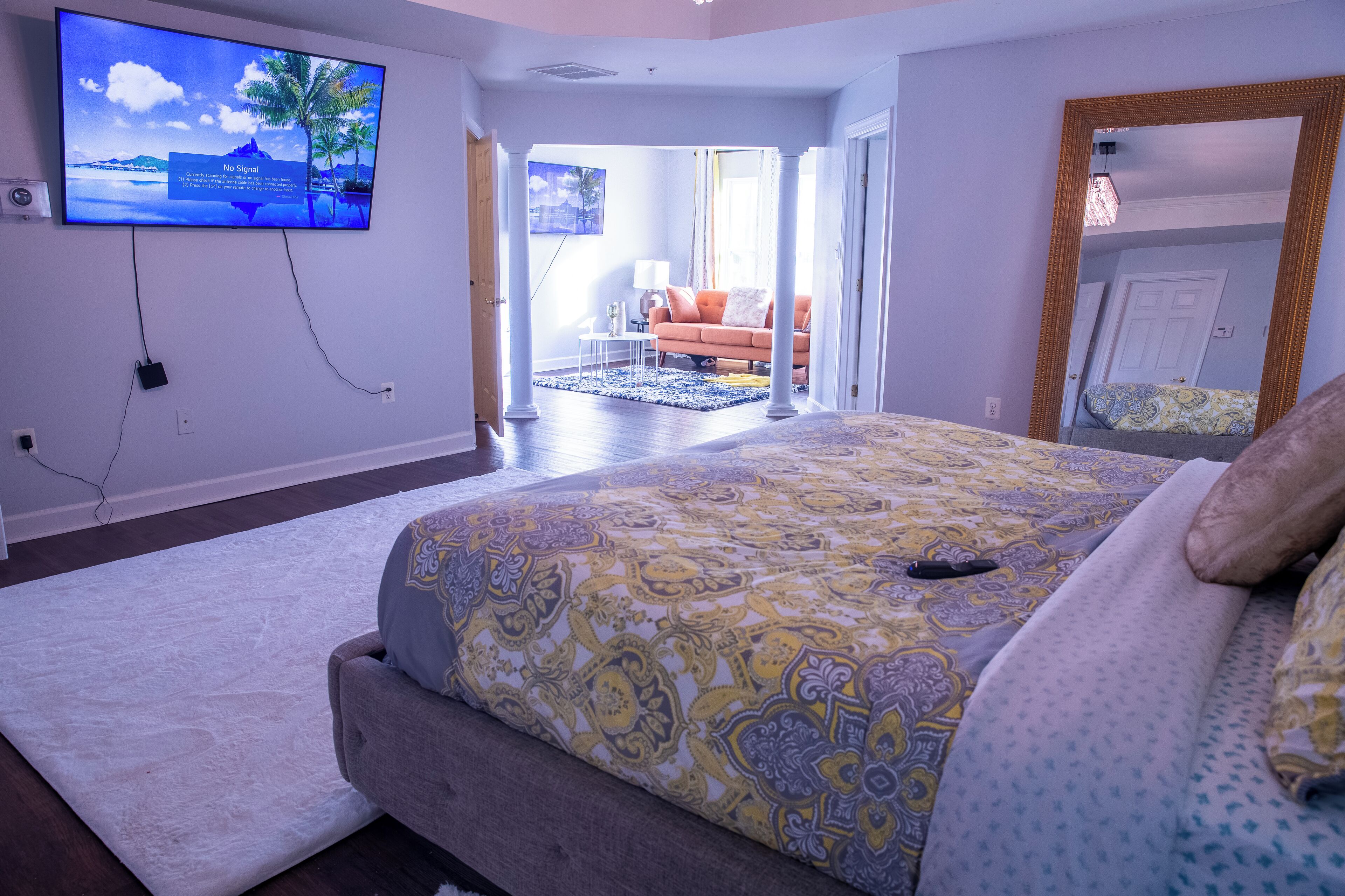A bedroom with a large bed, a television mounted on the wall, and a view into another room.