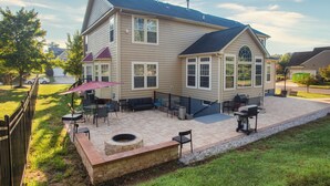 Une maison à deux étages dotée d’un patio aménagé avec des meubles d’extérieur, un barbecue et un foyer.