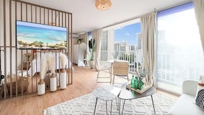 A modern living room with a large TV, a balcony with a city view, and a dining area. - Oceanview Remodeled Studio in the heart of Waikiki, walk to shops, food, & beach (Honolulu)