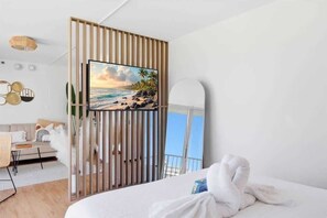 Ein Hotelzimmer mit Bett, Blick auf den Strand, einer Holzwand und einem an der Wand befestigten Fernseher.
