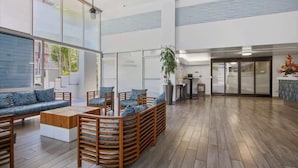 A spacious lobby with a wooden floor, a seating area with sofas and chairs, a large window, and a plant. - Oceanview Remodeled Studio in the heart of Waikiki, walk to shops, food, & beach (Honolulu)