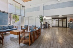 Eine geräumige Lobby mit Holzboden, einer Sitzecke mit Sofas und Sesseln, einem großen Fenster und einer Pflanze.