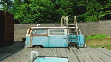 A blue van with a ladder, a wooden deck, and a swimming pool.