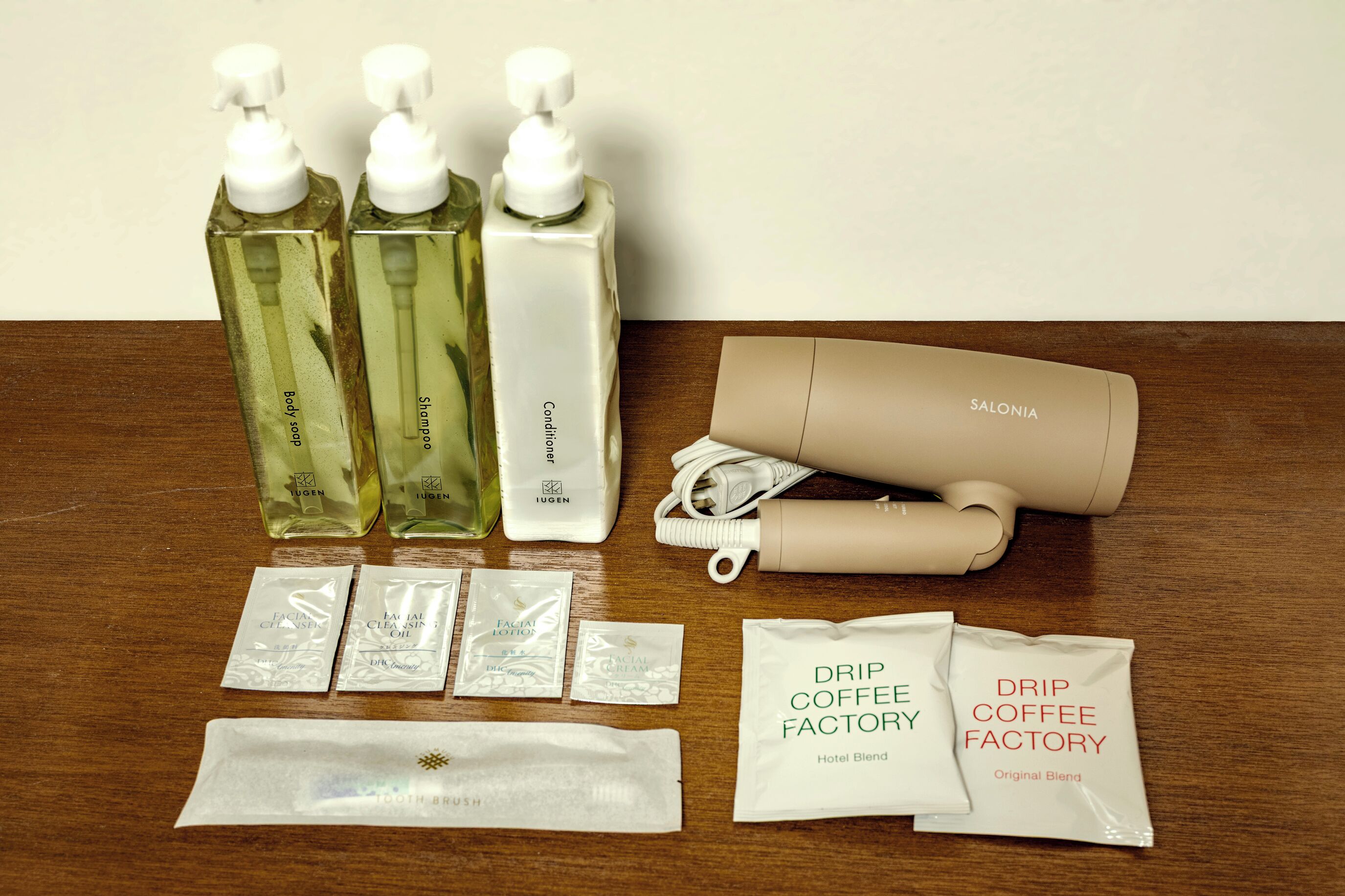 A table with various toiletries including body soap, shampoo, conditioner, a hair dryer, facial cleansing oil, and coffee blends.