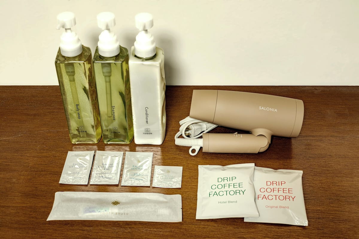 Een tafel met diverse toiletartikelen, waaronder douchezeep, shampoo, conditioner, een haardroger, gezichtsreinigingsolie en koffiemelanges.