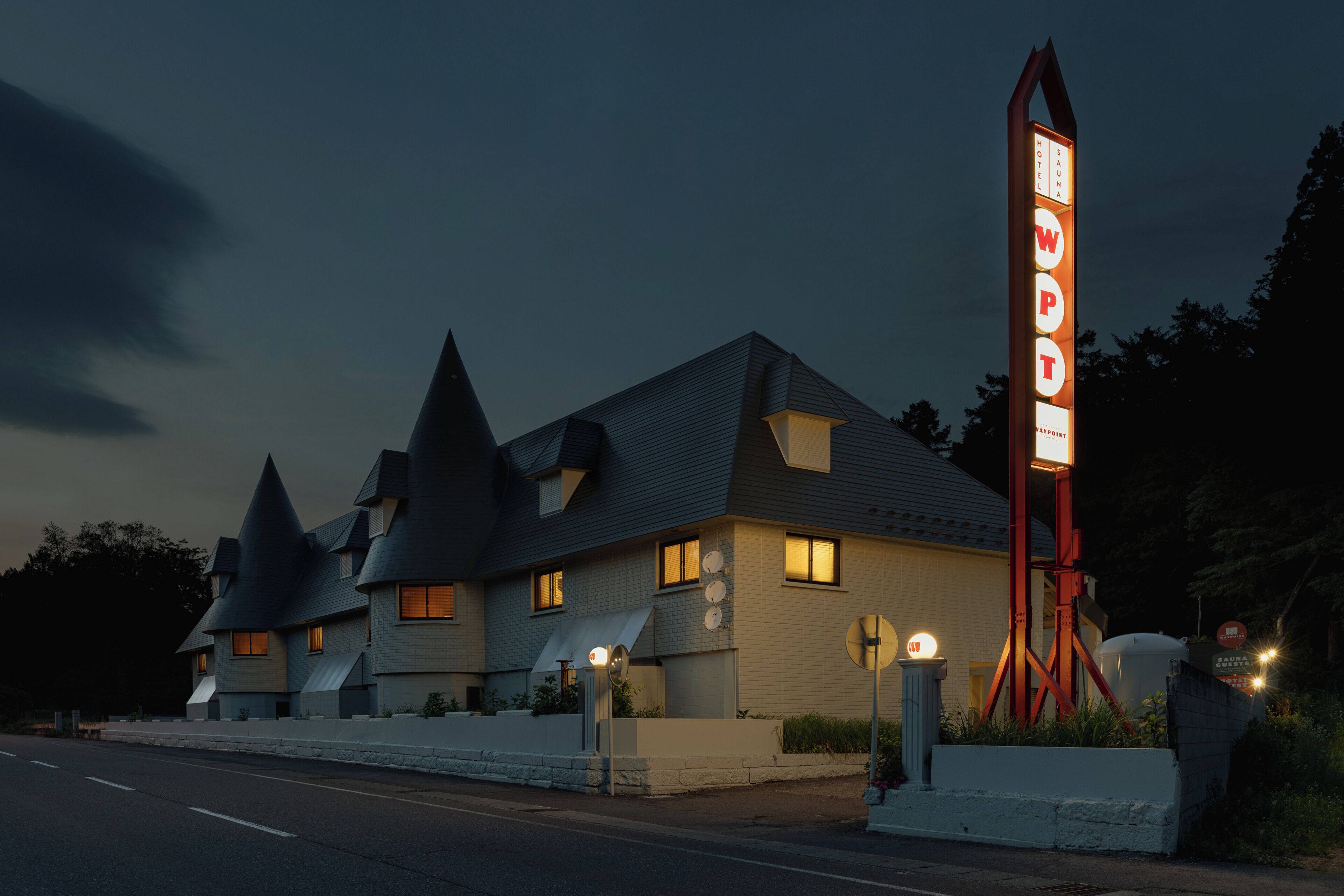 Um hotel com um letreiro alto e vermelho característico, e um edifício moderno com vários telhados em mansarda.