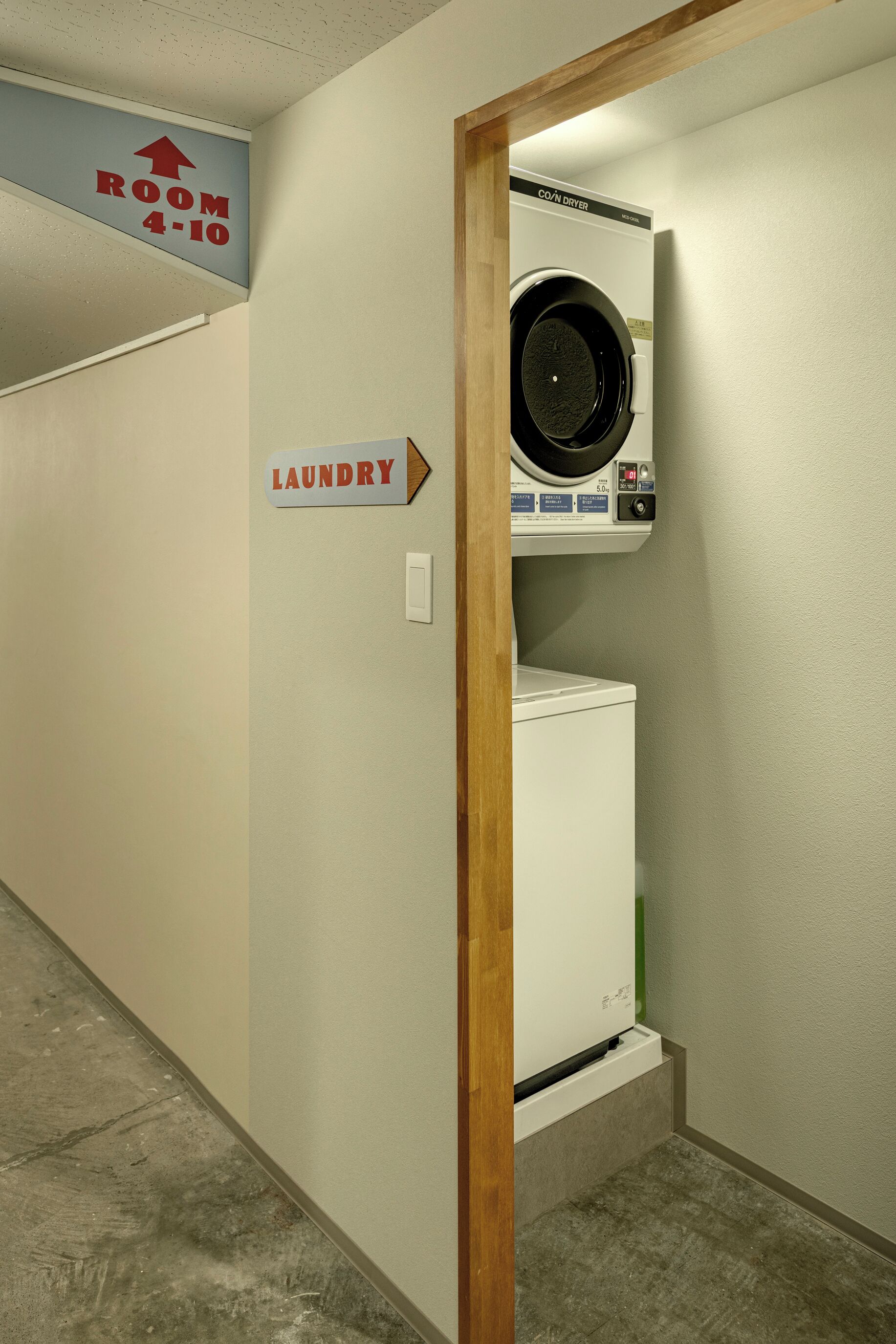 A laundry area with a washing machine and dryer, a sign indicating the direction to the laundry room, and a door leading to another room.