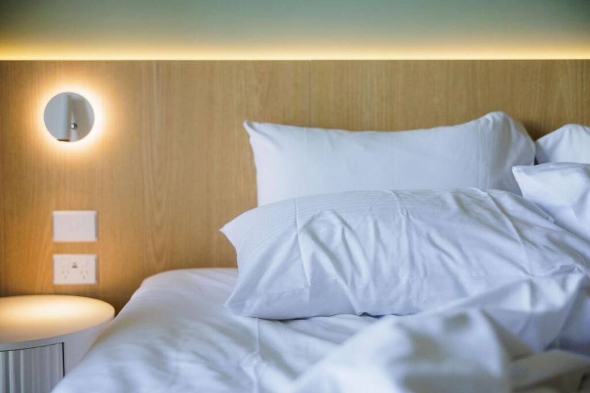A neatly made bed with white linens, a round wall mirror, and a bedside table with a light.