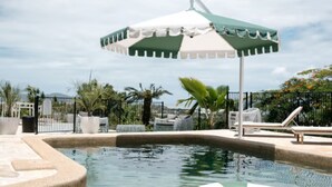 A swimming pool with a green and white inflatable ring, a white umbrella, and lounge chairs. - Victoria Street Boutique Hotel (Townsville City)