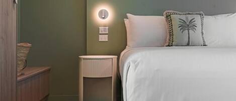 A bedroom with a bed, a nightstand, a wall-mounted light, and a small side table.