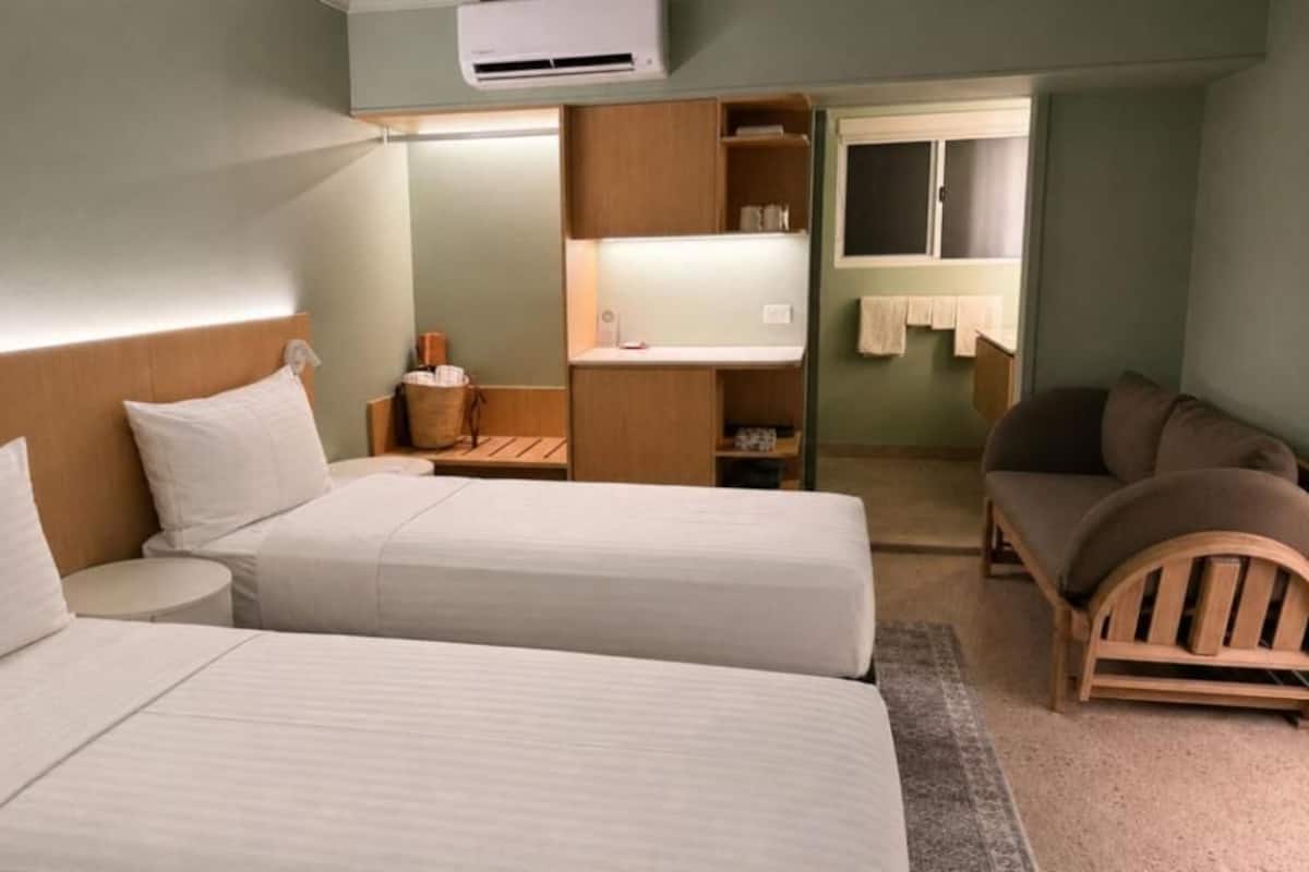 A hotel room with two beds, a small table, a sofa, and a window with a towel hanging.
