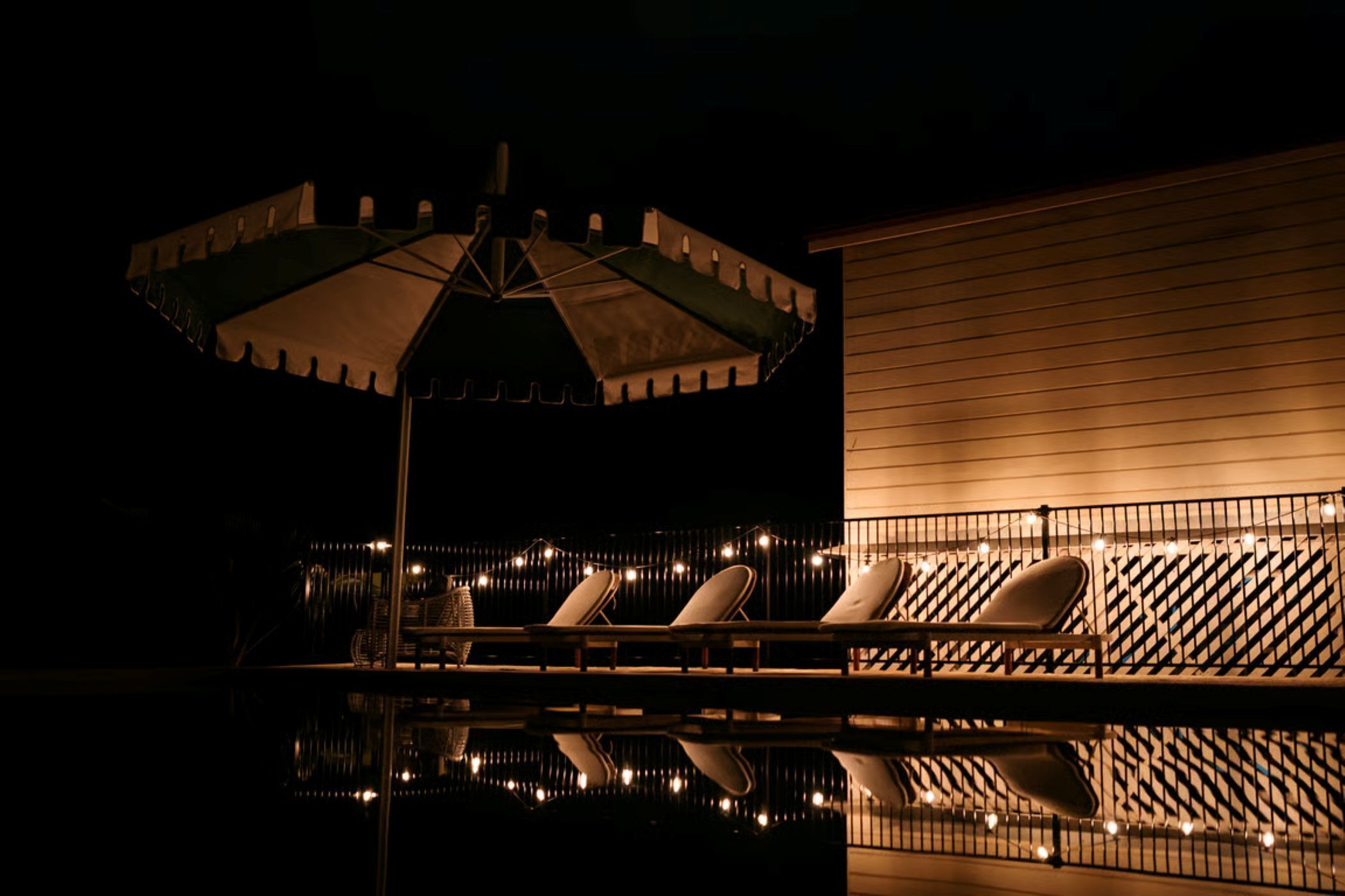 Un espace piscine aménagé pour la nuit, avec des chaises longues et un parasol.