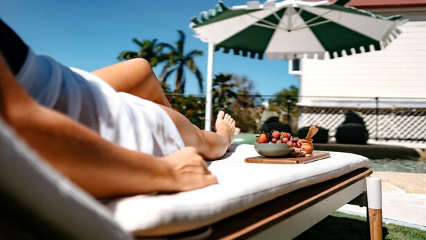 A person relaxing on a sun lounger with a bowl of fruit and a bottle of water. - Victoria Street Boutique Hotel (Townsville City)