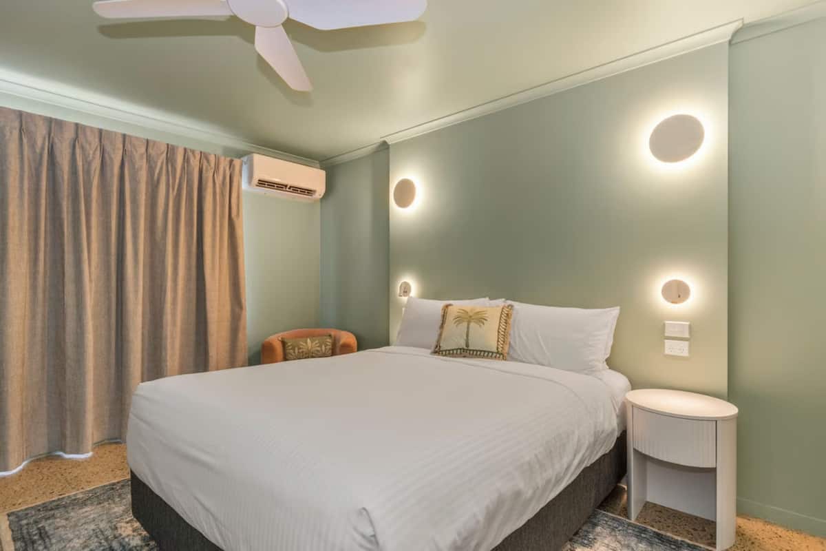 A bedroom with a large bed, a ceiling fan, a nightstand, and a wall-mounted air conditioner.