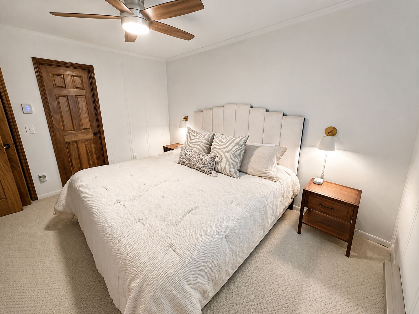 Un dormitorio con una cama, ventilador de techo, mesita de noche y lámpara de pared.