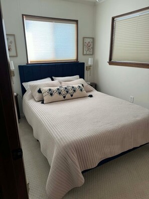 A bedroom with a large bed, a blue headboard, and a window with blinds. - Summit 101B: 3 Bedrooms 2 Full Baths (Snowshoe)