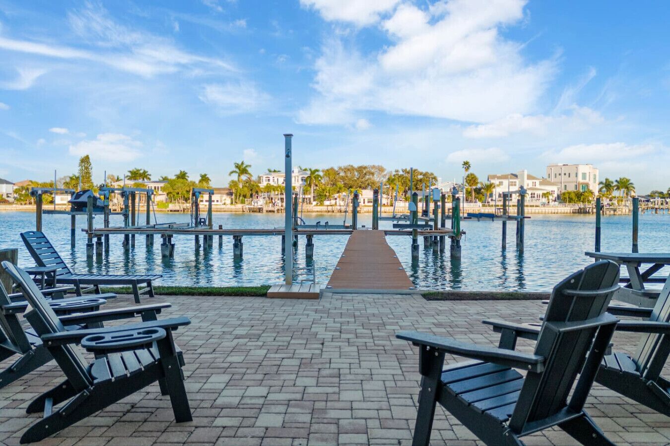 A waterfront patio with lounge chairs and a dock extending into the water.