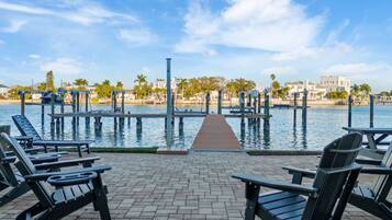 A waterfront patio with lounge chairs and a dock extending into the water.