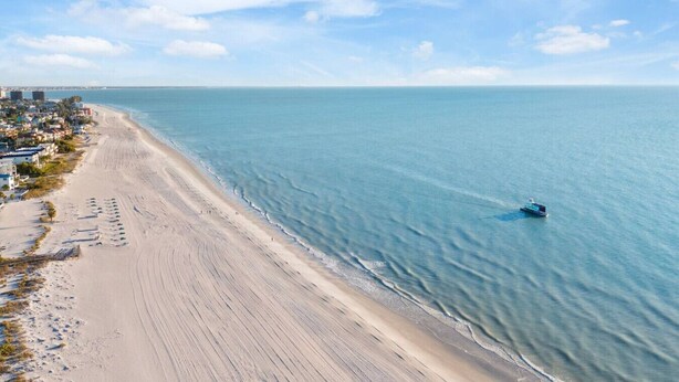 A coastal beach with a clear view of the ocean and a small boat. - 3BR Water View Condo | Boat Access+Great Location (Treasure Island)