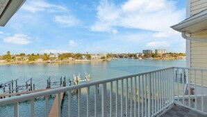 A waterfront view from a balcony with a railing, a dock, and buildings in the background. - 3BR Water View Condo | Boat Access+Great Location (Treasure Island)