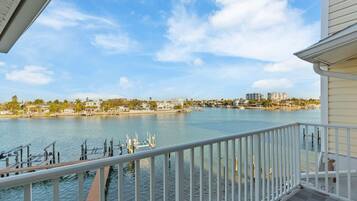 A waterfront view from a balcony with a railing, a dock, and buildings in the background.