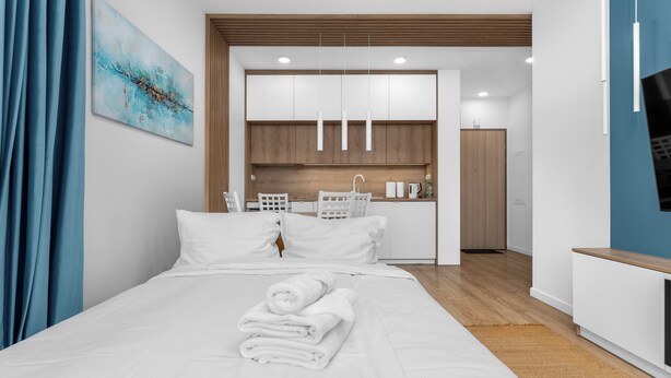 Quarto de hotel moderno com uma cama bem arrumada, uma pequena cozinha e vista para o banheiro próximo.