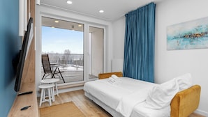 Quarto de hotel moderno com cama, mesa pequena com cadeiras, televisão e vista para o exterior.