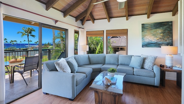 A modern living room with a large gray sectional sofa, a glass coffee table, and a ceiling fan. - Luxury Ocean-View 2BR Condo | Walk to Poipu Beach | Sleeps 6 (Koloa)