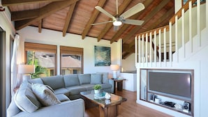 A living room with a sectional sofa, a coffee table, a TV, and a staircase. - Luxury Ocean-View 2BR Condo | Walk to Poipu Beach | Sleeps 6 (Koloa)