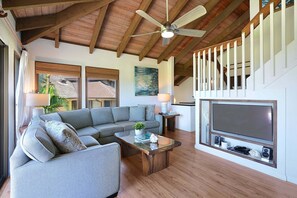 A living room with a sectional sofa, a coffee table, a TV, and a staircase. - Luxury Ocean-View 2BR Condo | Walk to Poipu Beach | Sleeps 6 (Koloa)