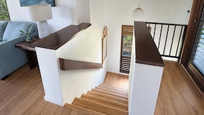 A staircase with wooden steps and white walls, leading to a balcony with a railing. - Luxury Ocean-View 2BR Condo | Walk to Poipu Beach | Sleeps 6 (Koloa)